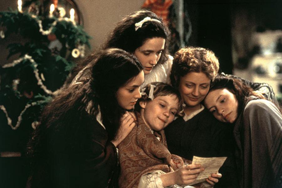 Screen still from Gillian Armstrong's 1994 Little Women featuring the March sisters and their mother huddled together while reading a letter from their father on Christmas